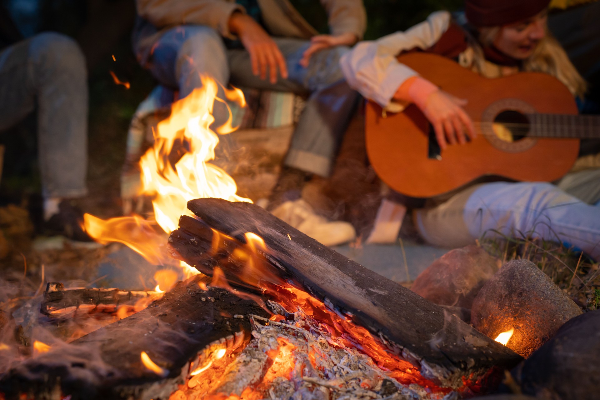Unrecognizable friends having fun playing music and enjoying bonfire camping in nature at night